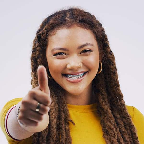 Smiling young woman with braids and braces points at the viewer in a yellow top.